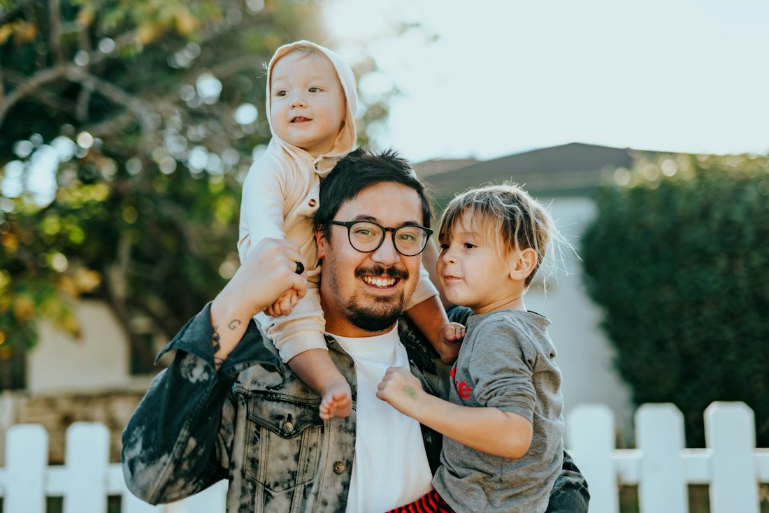 Dad with two kids in front of a white fence